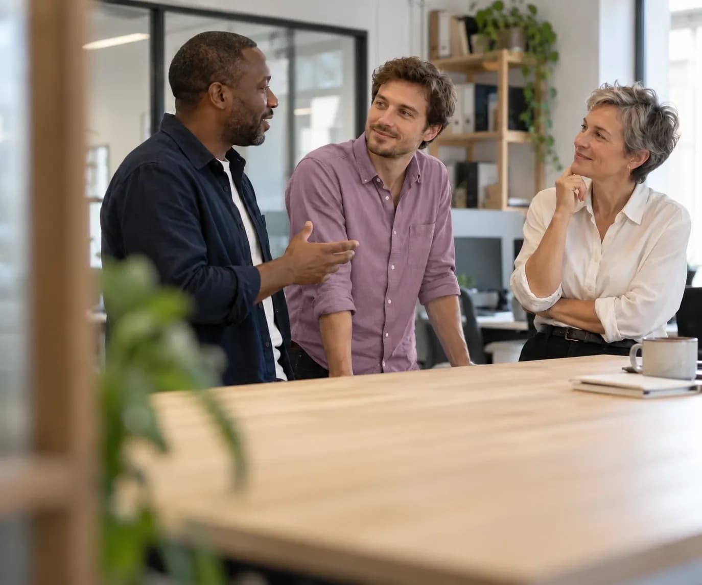 Trois collègues discutent debout autour d’une table de travail