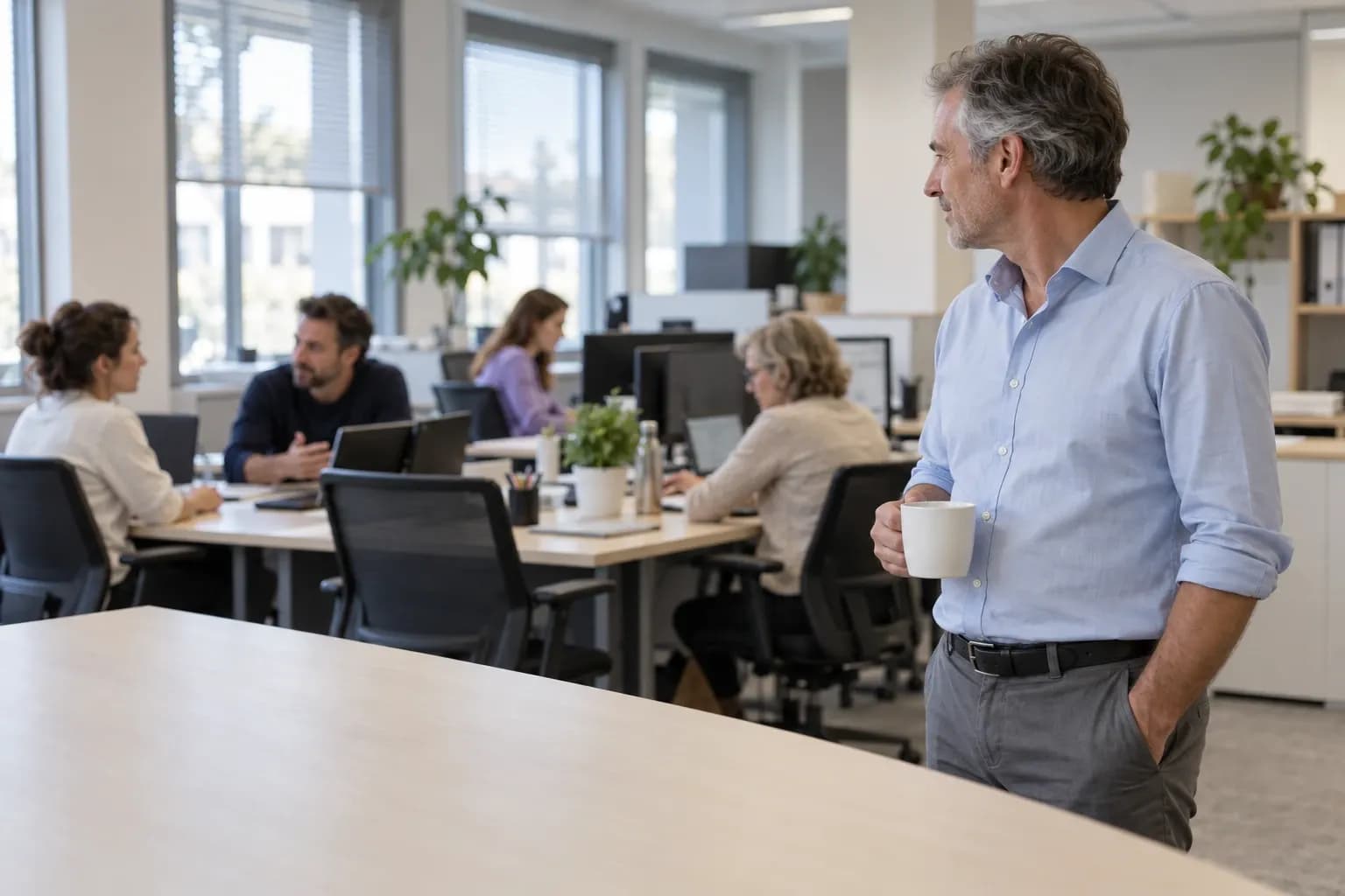 Un dirigeant, une tasse à la main, observe son équipe au travail dans un open space
